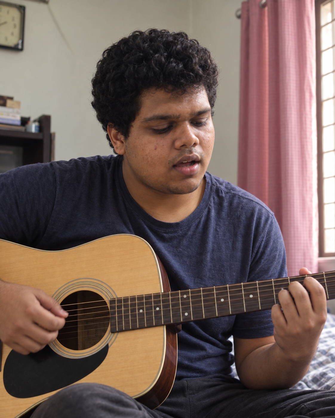 Conceptual candid-style portrait of Yethikrishna R singing and playing an acoustic guitar beside a window in a home setting.
